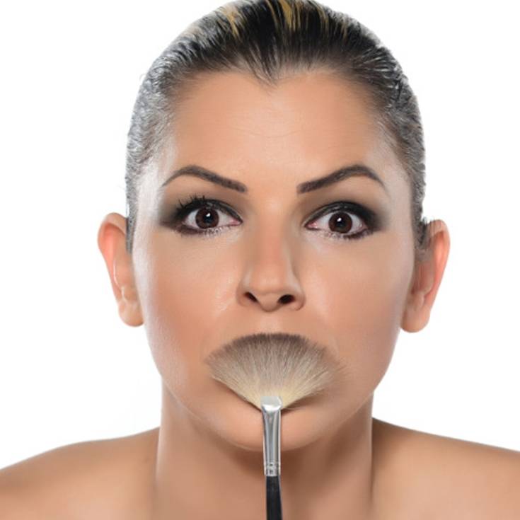 Mulher surpresa com um pincel de maquiagem na boca